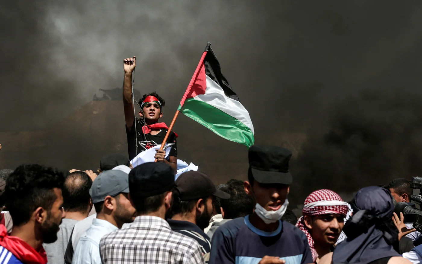 Un manifestant palestinien agite son drapeau national alors que la fumée s’élève de pneus en feu lors d’une manifestation le long de la frontière entre la bande de Gaza et Israël, le 8&nbsp;juin&nbsp;2018 (AFP)