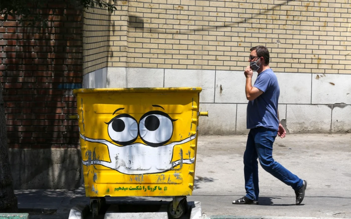 Un Iranien passe devant une poubelle de rue, peinte d’un dessin de masque dans une campagne de sensibilisation à la pandémie de coronavirus COVID-19, Téhéran le 18 juillet 2020 (AFP)