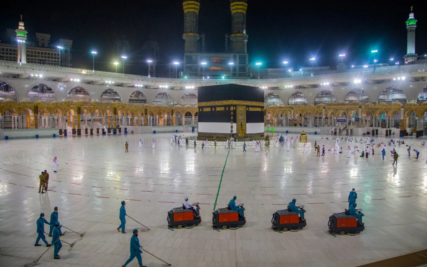 Des travailleurs en train de nettoyer tandis que quelques pèlerins prient devant la Kaaba, le 27 juillet 2020 (AFP)