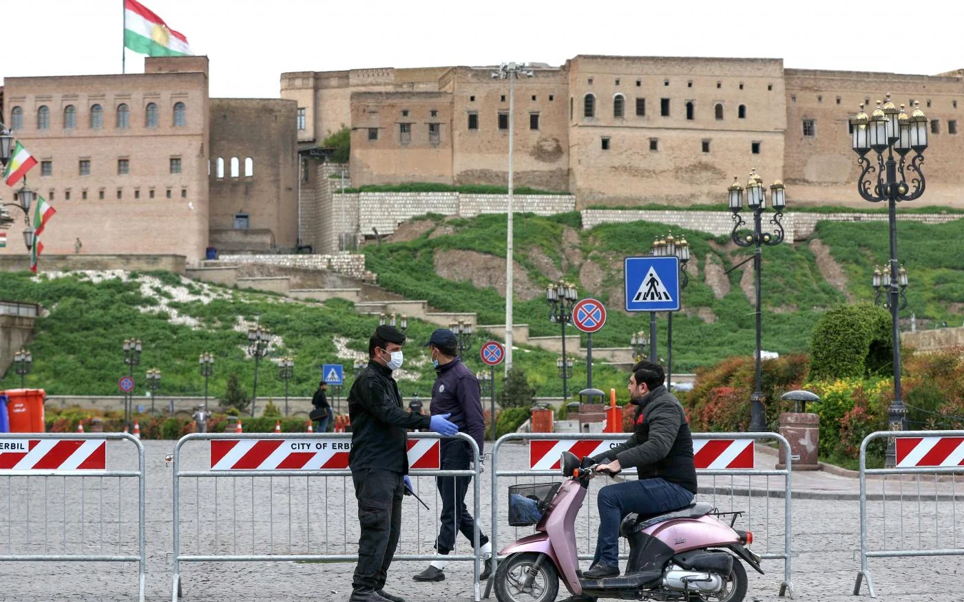 Un agent de sécurité portant des gants de protection et un masque s’approche d’un homme à moto devant la citadelle d’Erbil (AFP)