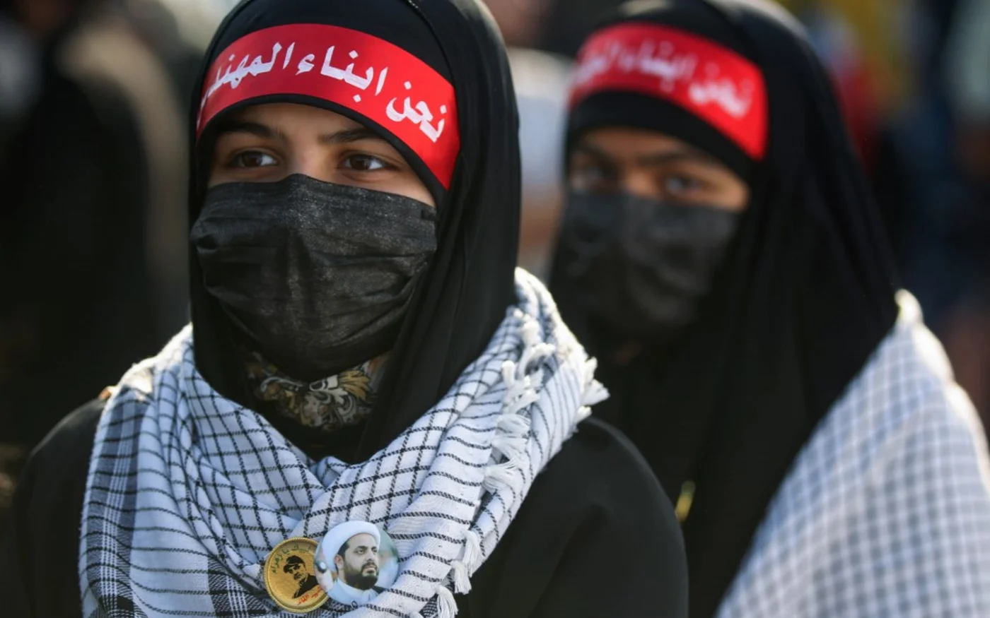 Des Irakiennes portent des bandeaux indiquant : « Nous sommes les enfants d’al-Mouhandis » et des badges représentant les portraits de Qasem Soleimani (à gauche) à Bagdad le 3 janvier 2021 (AFP)