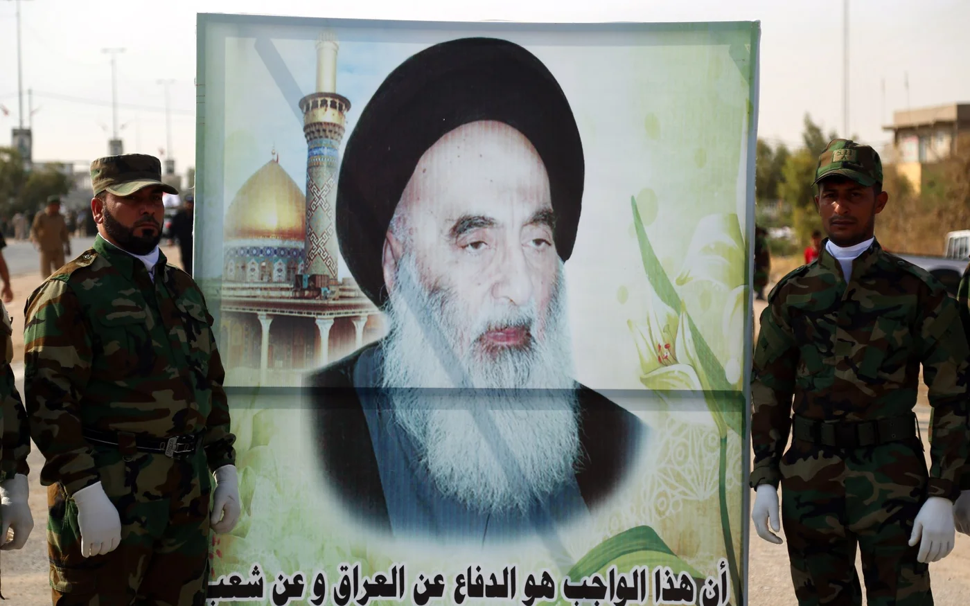 Des membres des Unités de mobilisation populaire portant une grande banderole représentant l’image du dignitaire chiite, l’ayatollah Ali al-Sistani, à Nadjaf (AFP)