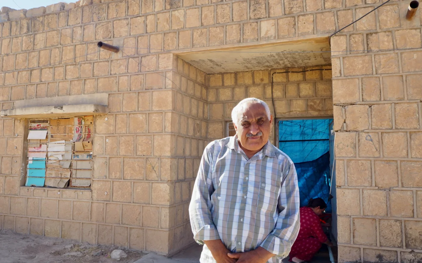 Hani Ellias al-Saigh se tient devant le modeste trois pièces familial, situé dans une rangée d’anciens quartiers militaires à Sinouni, dans la région irakienne du Sinjar (MEE/Tom Westcott)