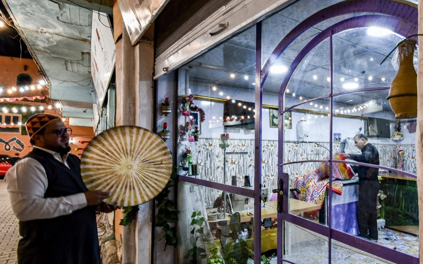 Un homme joue du tambourin devant l’échoppe d’un couturier à Mossoul, en Irak (AFP)