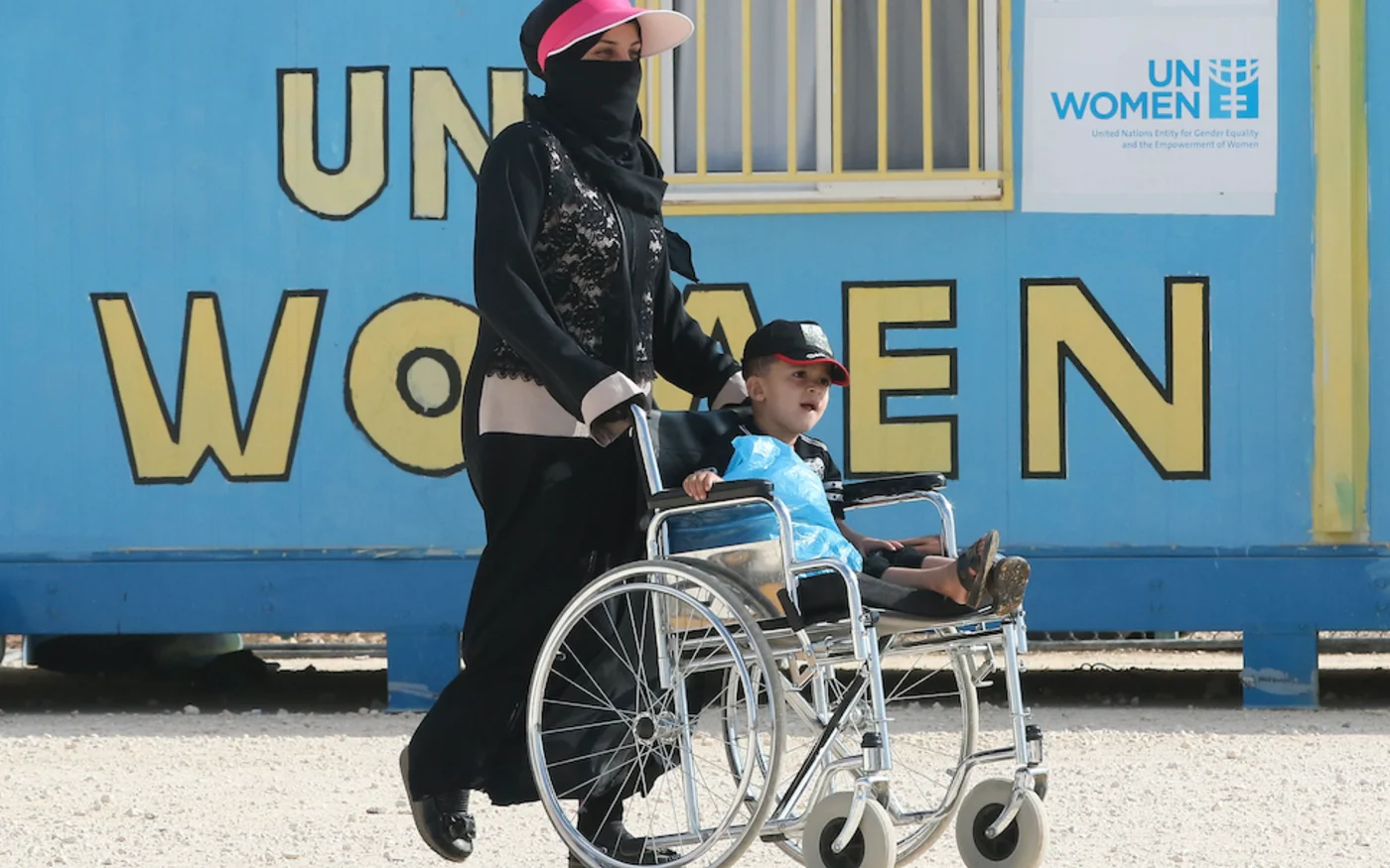 Une réfugiée syrienne pousse un enfant en fauteuil roulant, au camp de réfugiés d'Azraq, dans le nord de la Jordanie, le 2 août 2018 (AFP)