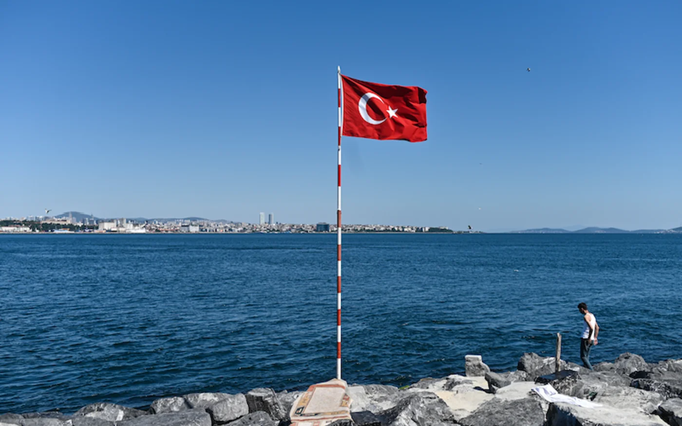 Un homme marche sur des rochers à côté d'un drapeau national turc, au bord du détroit du Bosphore, à Istanbul, le 28 juin 2020 (AFP)