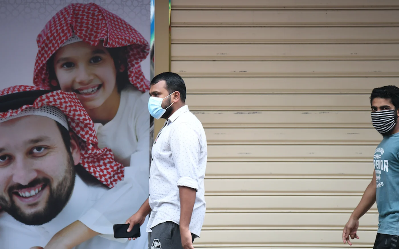 Des hommes passent devant une affiche, à Dubaï, le 15 avril 2020 (AFP)