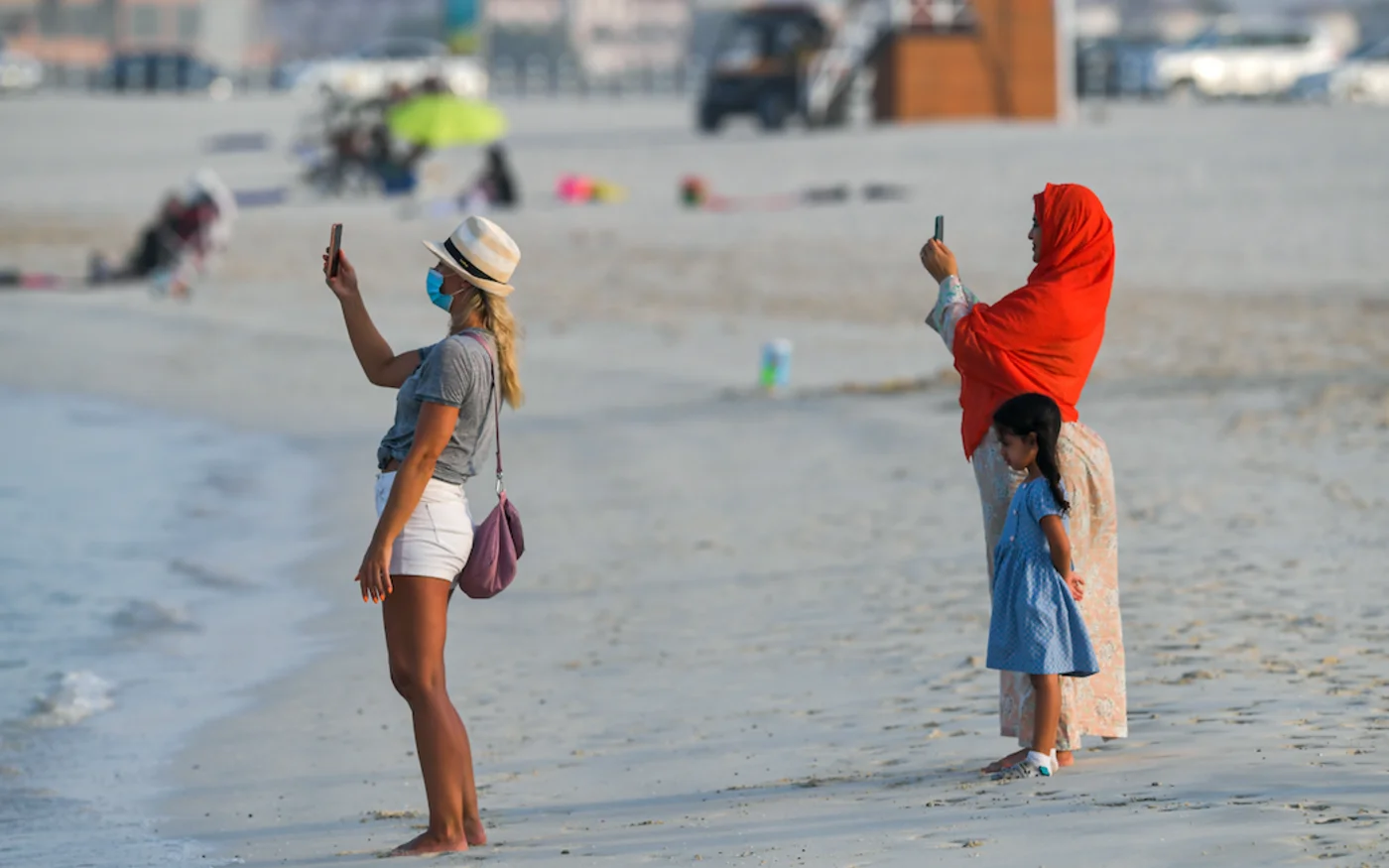 Une femme émiratie et une résidente étrangère prennent une photo, sur une plage, à Dubaï, le 25 juin 2020 (AFP)
