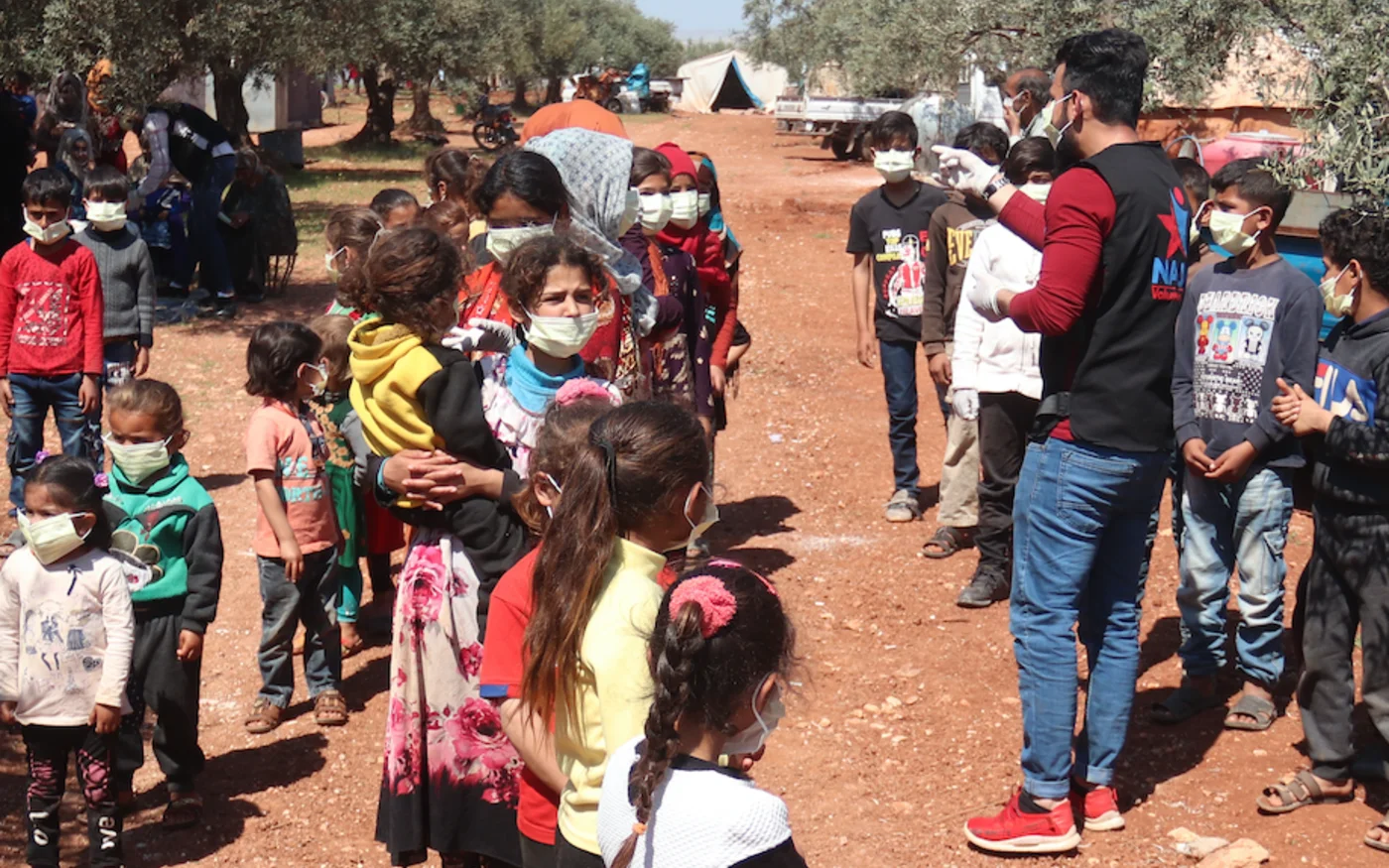 Des enfants écoutent un volontaire expliquer les mesures de protection contre la propagation du coronavirus, dans un camp pour Syriens déplacés, au nord d'Idleb, le 14 avril 2020 (AFP)