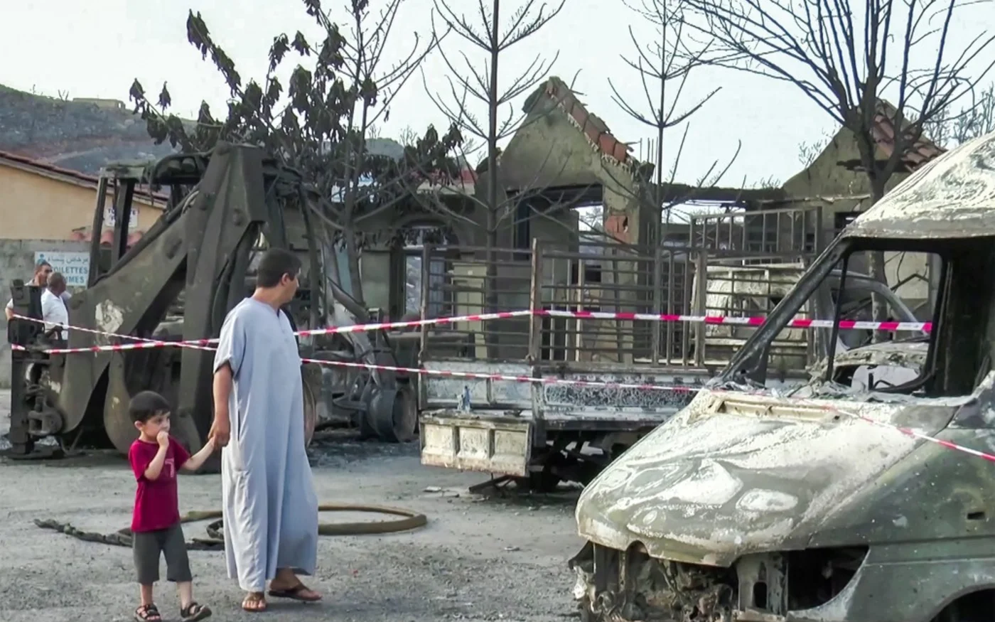 Un homme et un enfant inspectent les dommages causés aux véhicules et bâtiments incendiés dans le village de Tighramt, dans la province de Béjaïa, au nord-est d’Alger, le 25 juillet 2023 (AFP)