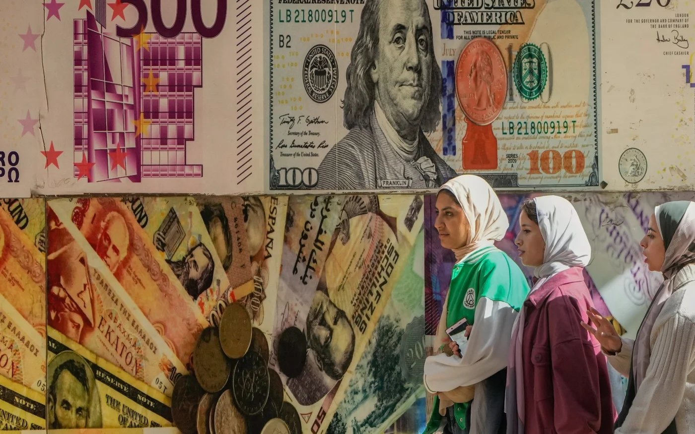 Des Égyptiennes passent devant un poster représentant le dollar américain et d’autres devises devant un bureau de change du Caire, le 12&nbsp;janvier&nbsp;2023 (AP)