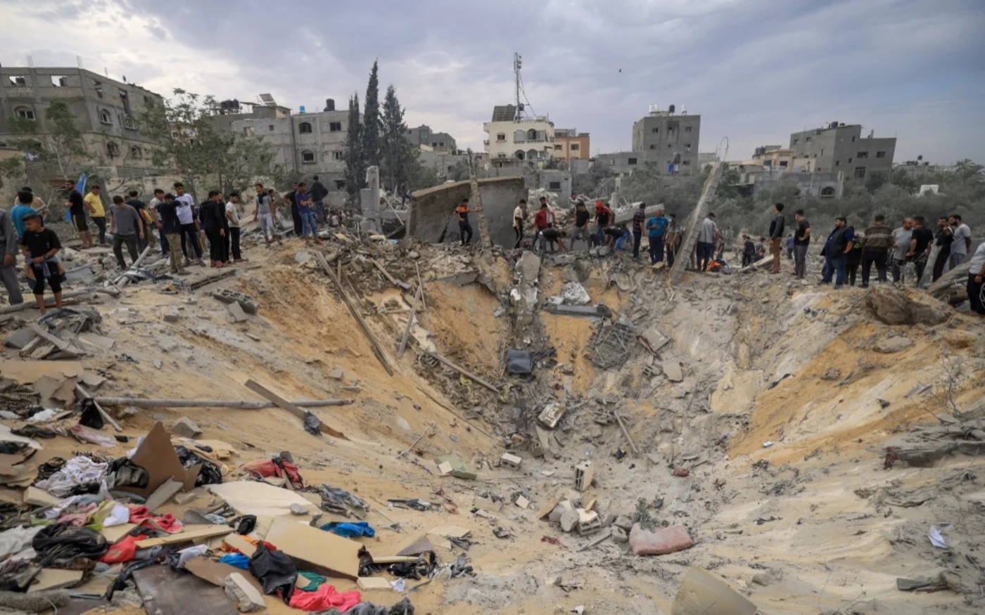 Des gens se tiennent devant un cratère provoqué par un bombardement israélien à Khan Younès, dans le sud de la bande de Gaza, le 12 novembre 2023 (AFP/Mahmud Hams)