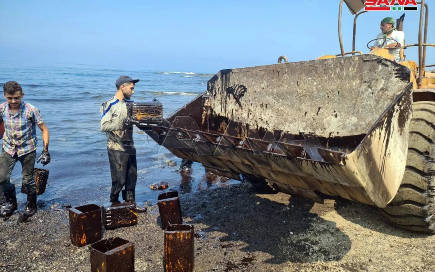 Des ouvriers syriens nettoient la marée noire avec des seaux en métal et une pelleteuse près de la centrale électrique de Banias, le 28 août 2021 (capture d’écran)