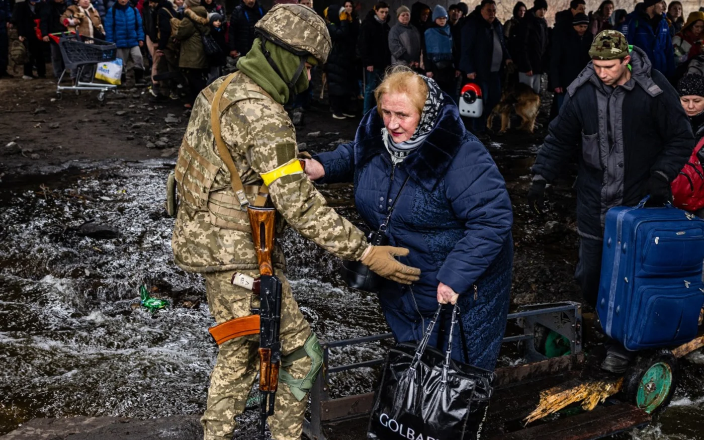 Un soldat ukrainien aide les personnes évacuées, rassemblées sous un pont détruit, qui fuient le bombardement d’Irpin, le 7 mars 2022 (AFP)