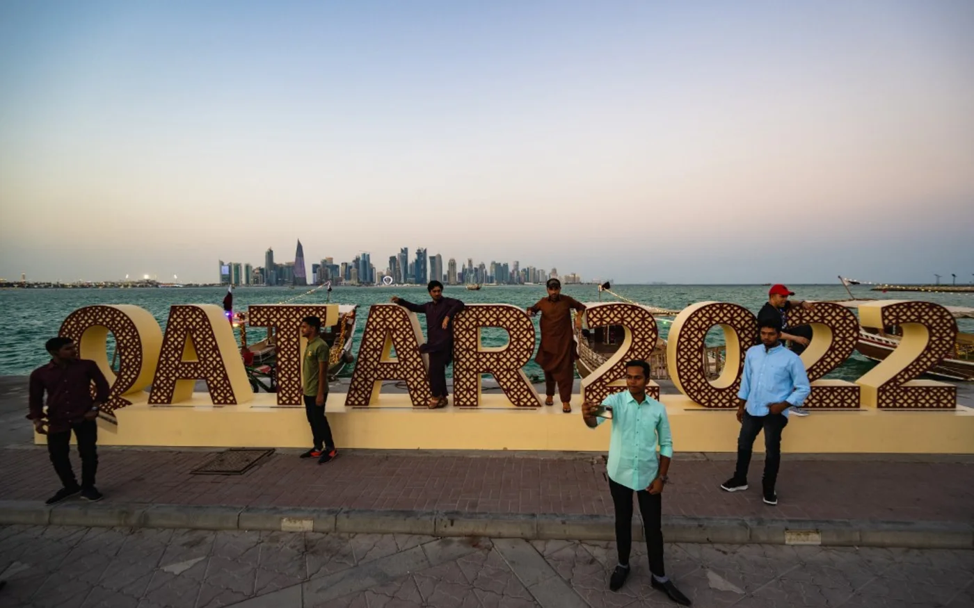 Des Qataris posent devant une installation consacrée à la Coupe du monde, à Doha, le 14 novembre 2022 (AFP/Andrej Isakovic)