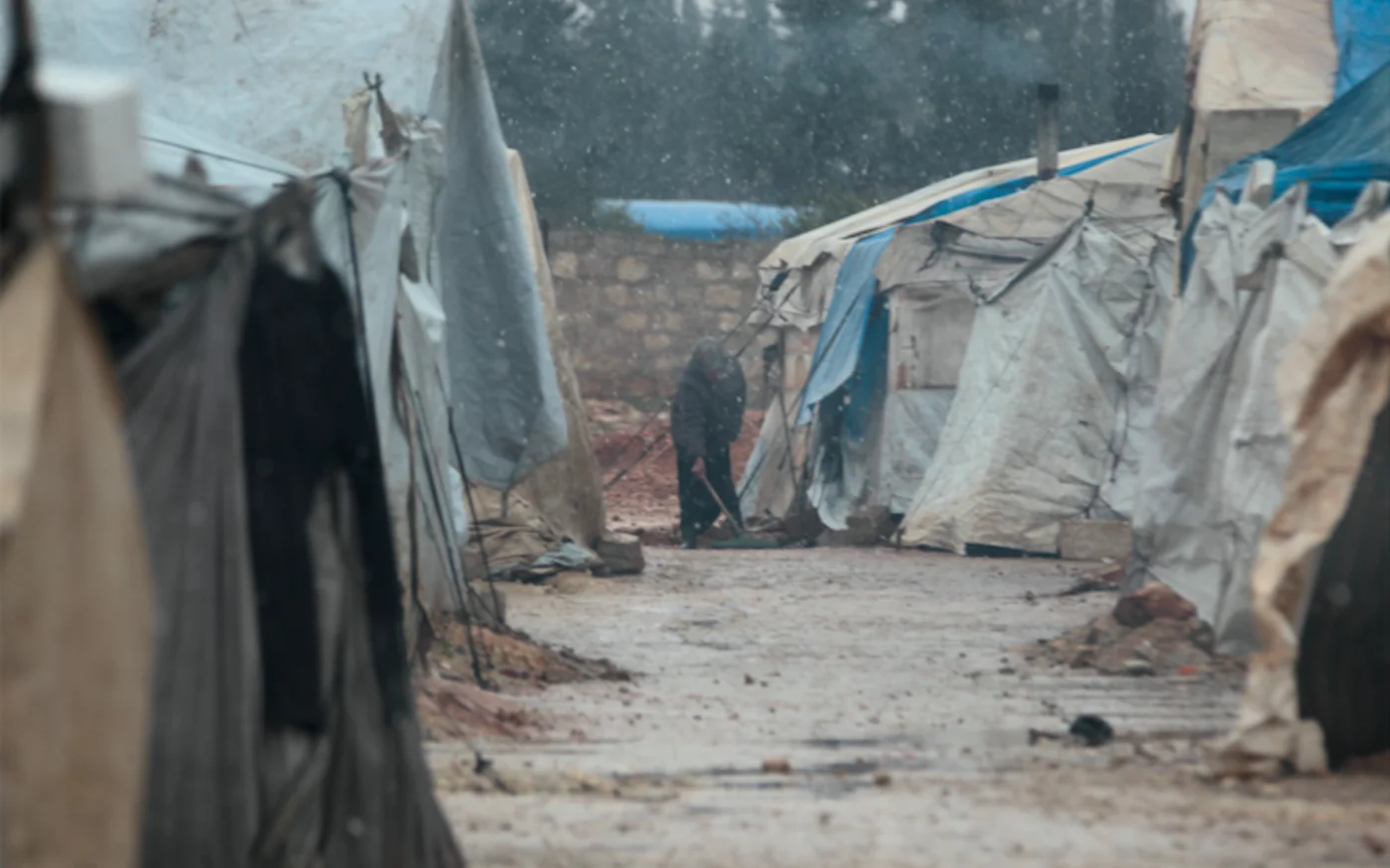 Une Syrienne nettoie le sol à l'extérieur d'une tente sous la neige dans un camp de déplacés syriens dans la campagne orientale de la province d'Alep (AFP)