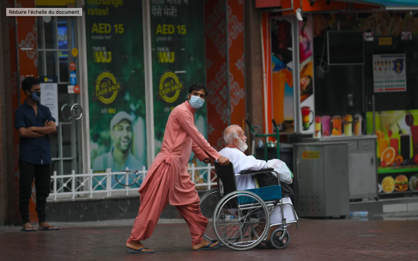 Un travailleur immigré pousse un homme en fauteuil roulant vers un centre de dépistage du coronavirus, à Dubaï, le 15 avril 2020 (AFP)