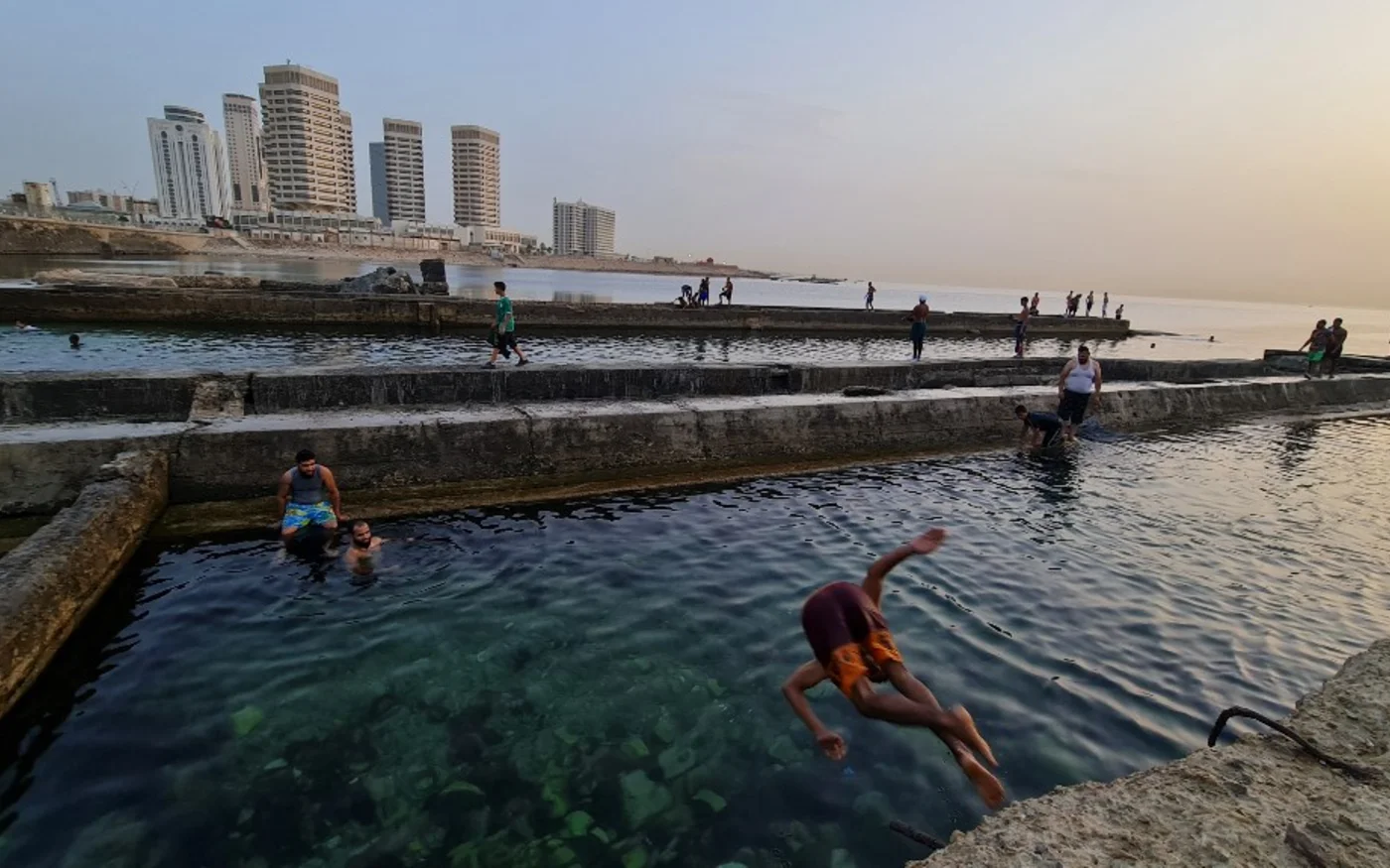 Des jeunes plongent dans la mer Méditerranée au coucher du soleil près des tours Dhat el-Emad à Tripoli, le 28 juin 2021 (AFP)