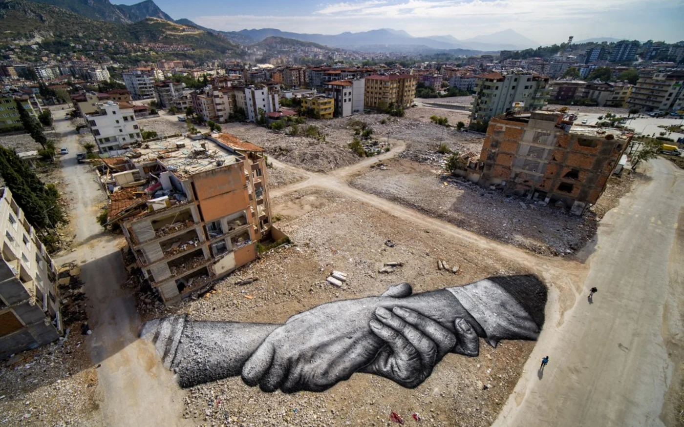 Cette photographie aérienne prise le 5 octobre 2023 à Antakya montre une peinture landart géante biodégradable située entre des bâtiments endommagés par l’artiste franco-suisse Guillaume Legros, dit Saype. La fresque en noir et blanc – deux mains entrelacées, sa marque de fabrique – s’étend sur 1 000 m2 là où se dressaient jusqu’à la nuit du 6 février 2023 des immeubles de quatre à cinq étages (AFP)