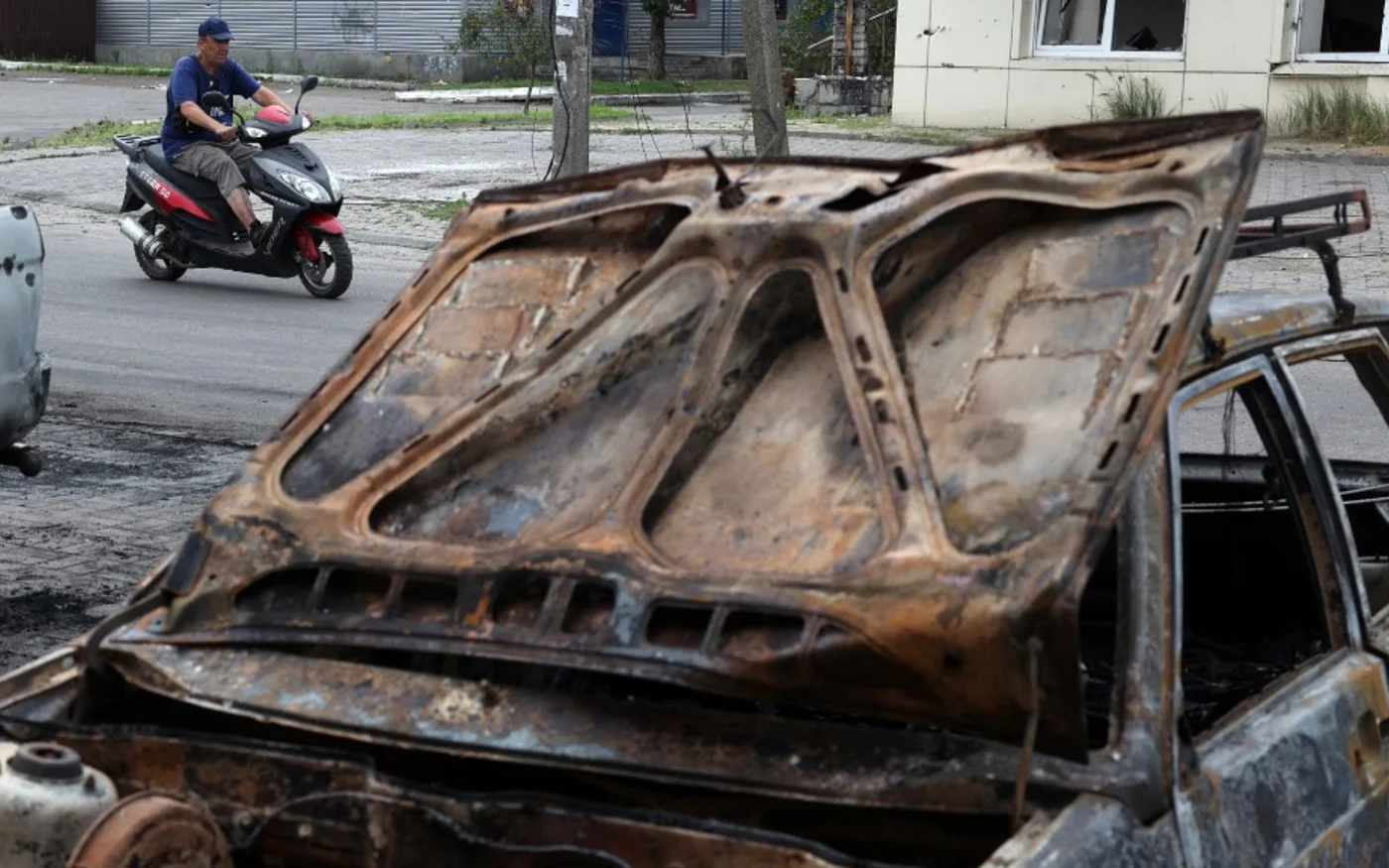 Un homme passe en scooter devant des voitures détruites par une frappe de missile à sous-munitions à Lyman, dans la région ukrainienne de Donetsk, le 8 juillet 2023 (AFP)