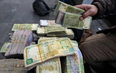 A currency trader sits by a stack of Syrian liras at his street stall in Damascus