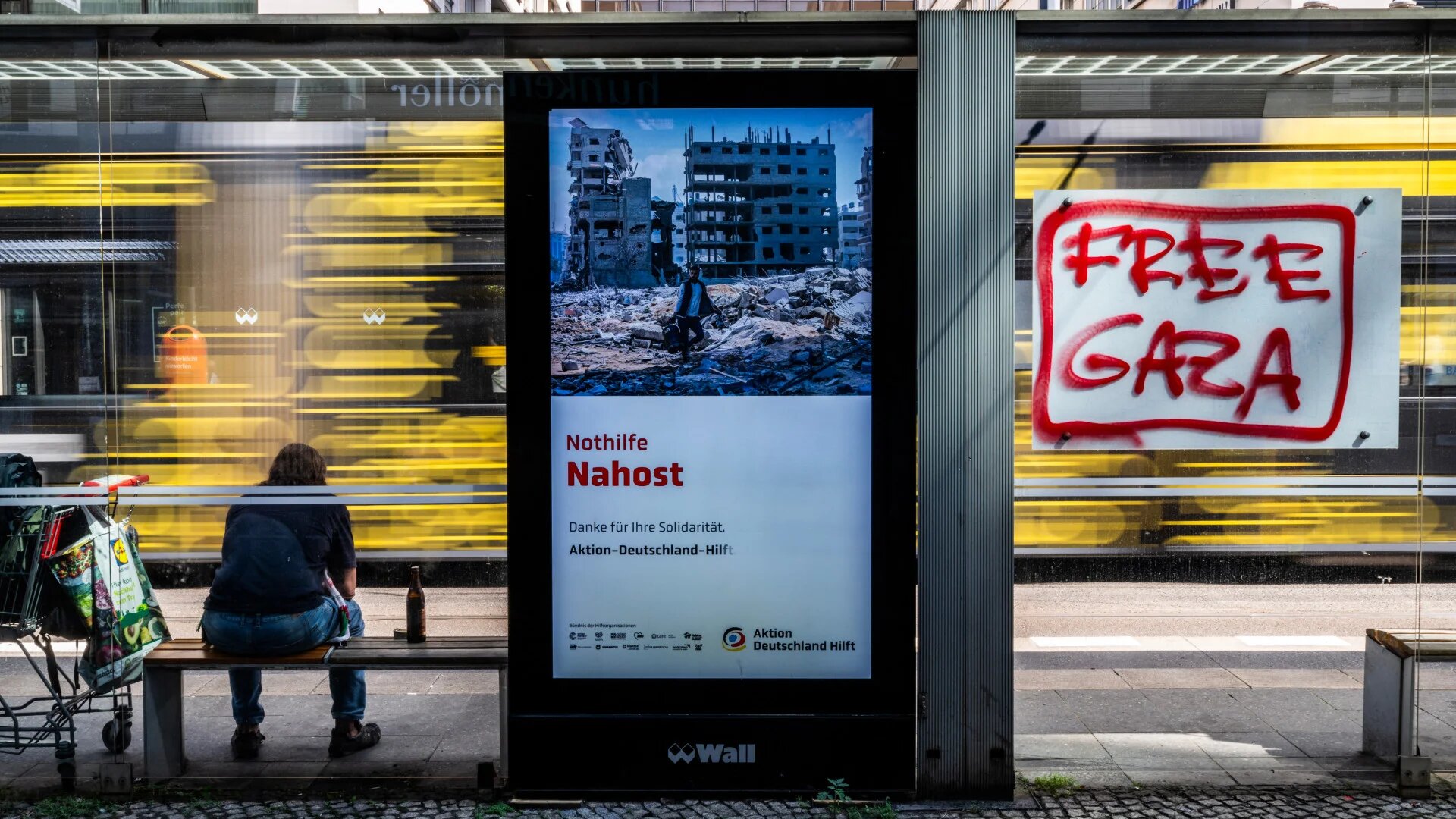 An advert for a German NGO offering aid in the Middle East appears next to graffiti reading "Free Gaza" at a tram stop in Berlin, 12 August 2025 (John MacDougall/AFP)