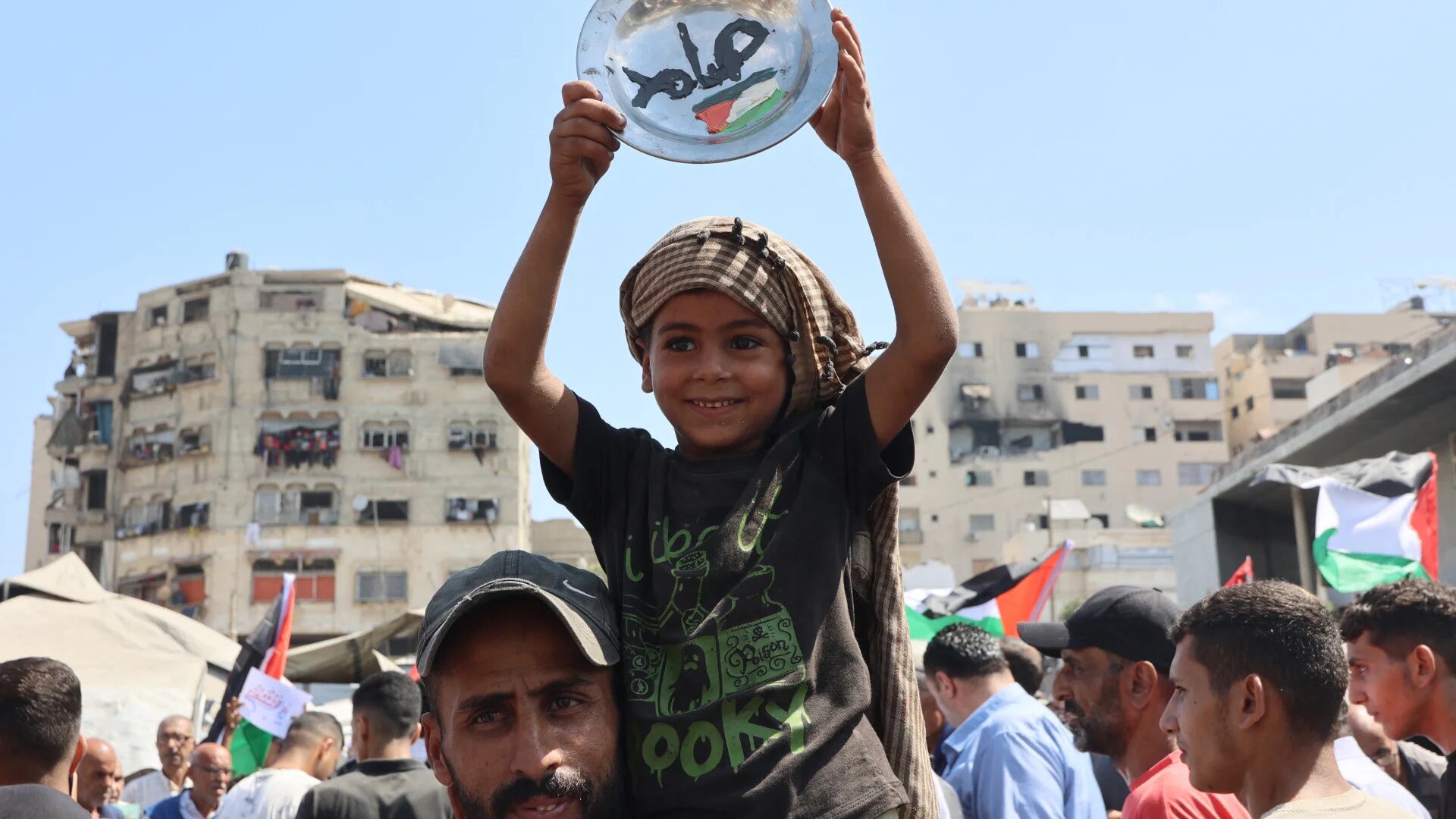 A Palestinian boy carries a plate with the Arabic word for steadfast during a demonstration in Gaza City calling for an end to Israel’s genocide, on 21 August 2025 (Omar Al-Qattaa/AFP)