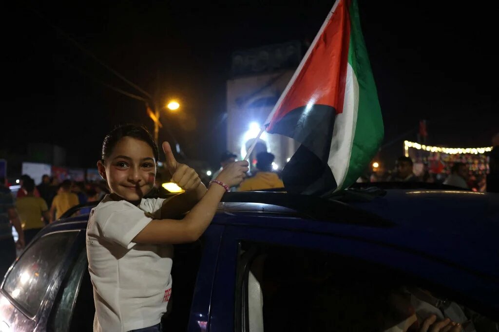 A child holds the Palestinian flag as she sits on the window sill of a car as people celebrate the ceasefire agreement in Khan Yunis, in the southern Gaza Strip.