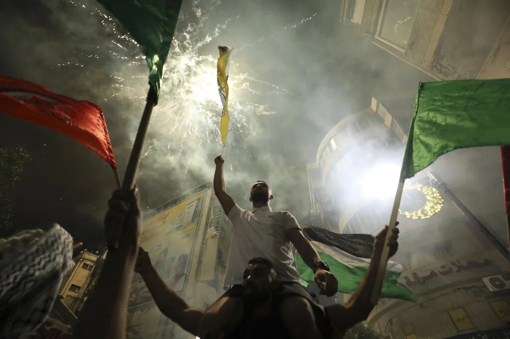 A man celebrates in the streets of Ramallah in the occupied West Bank as a firework lights up over him