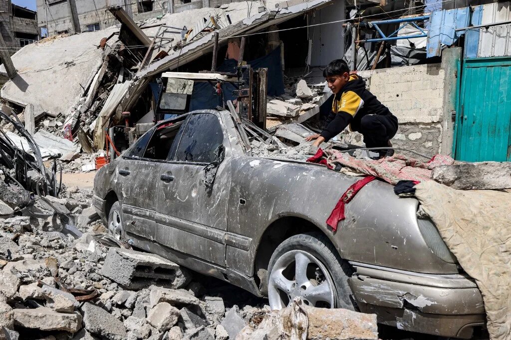 A boy clears rubble from atop a heavily damaged vehicle outside a destroyed building in Rafah in the southern Gaza Strip on April 5, 2024 amid the ongoing conflict in the Palestinian territory between Israel and the militant group Hamas. MOHAMMED ABED/AFP
