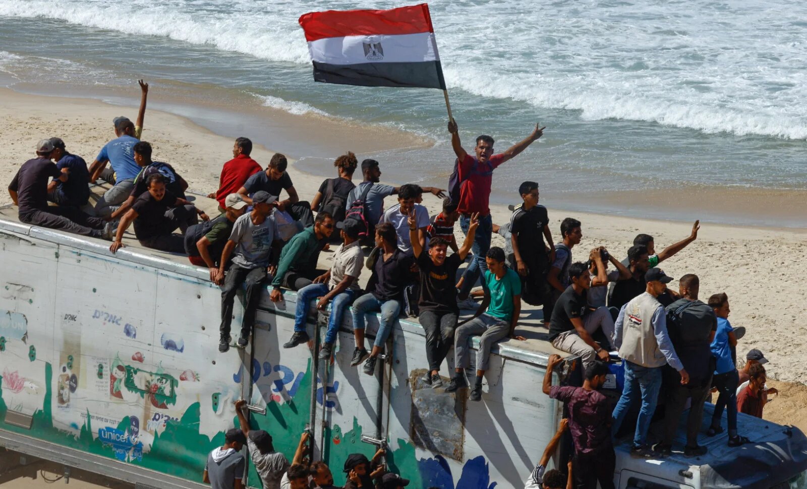 A man holds an Egyptian flag as Palestinians ride on a vehicle as they return to northern Gaza, 10 October 2025 (Mahmoud Issa/Reuters)