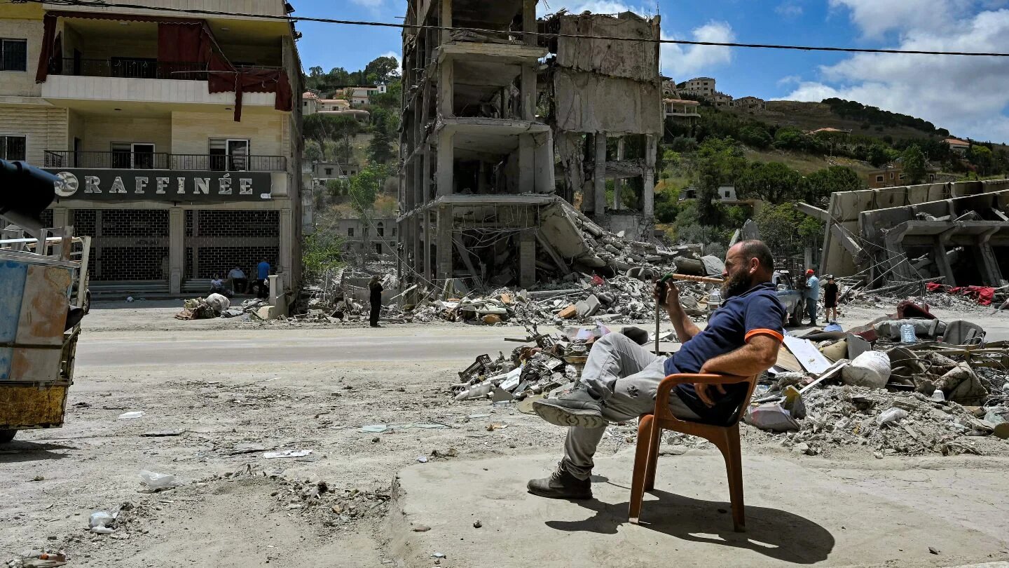 A man smokes a waterpipe while sitting beside rubble in the southern Lebanese town of Nabatieh al-Fawqa, 23 June 2026 (Fadel Itani/AFP)