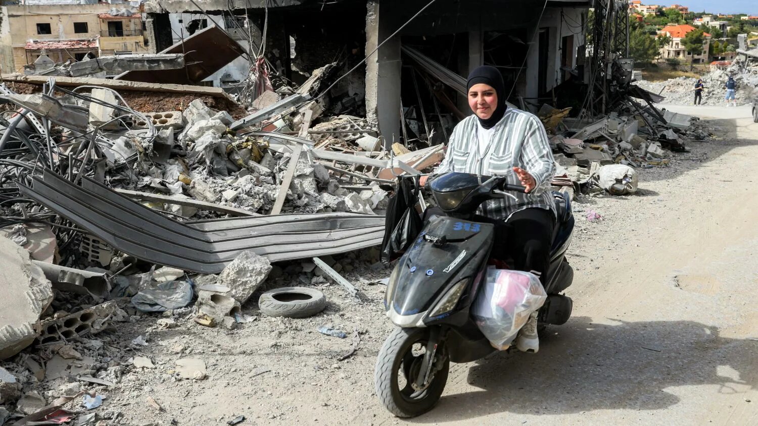 Woman rides scooter past destroyed building in Bir al-Salasel, southern Lebanon, 15 June 2026 (Mahmoud Zayyat/AFP)