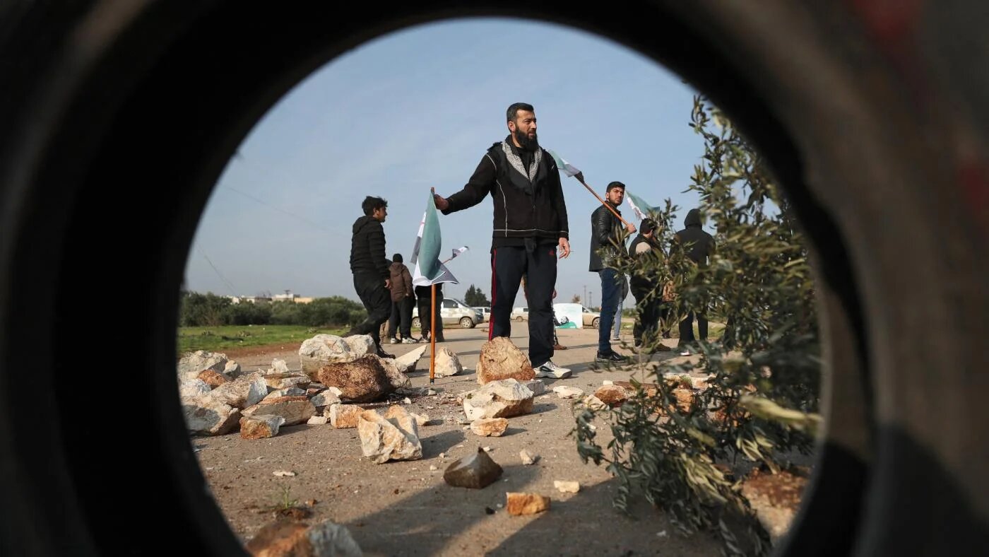 Des Syriens manifestent devant un véhicule militaire turc, avant l’arrivée de patrouilles conjointes turques et russes au sud-est de la ville d’Idleb, le 15 mars 2020 (AFP)