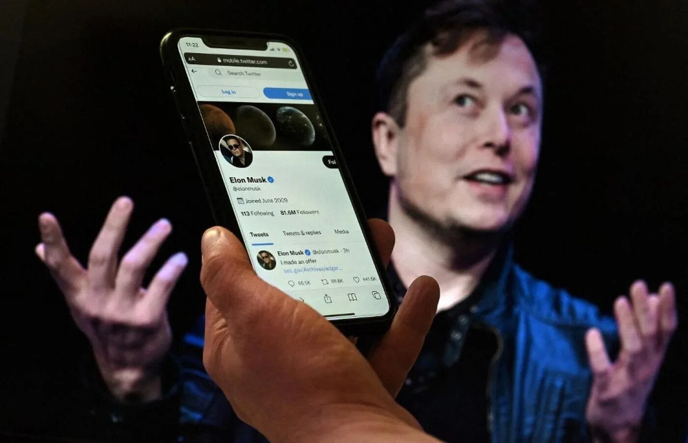 Un écran de téléphone affiche le compte Twitter d’Elon Musk tandis qu’une photo de lui est visible en arrière-plan, le 14 avril 2022 à Washington (AFP)