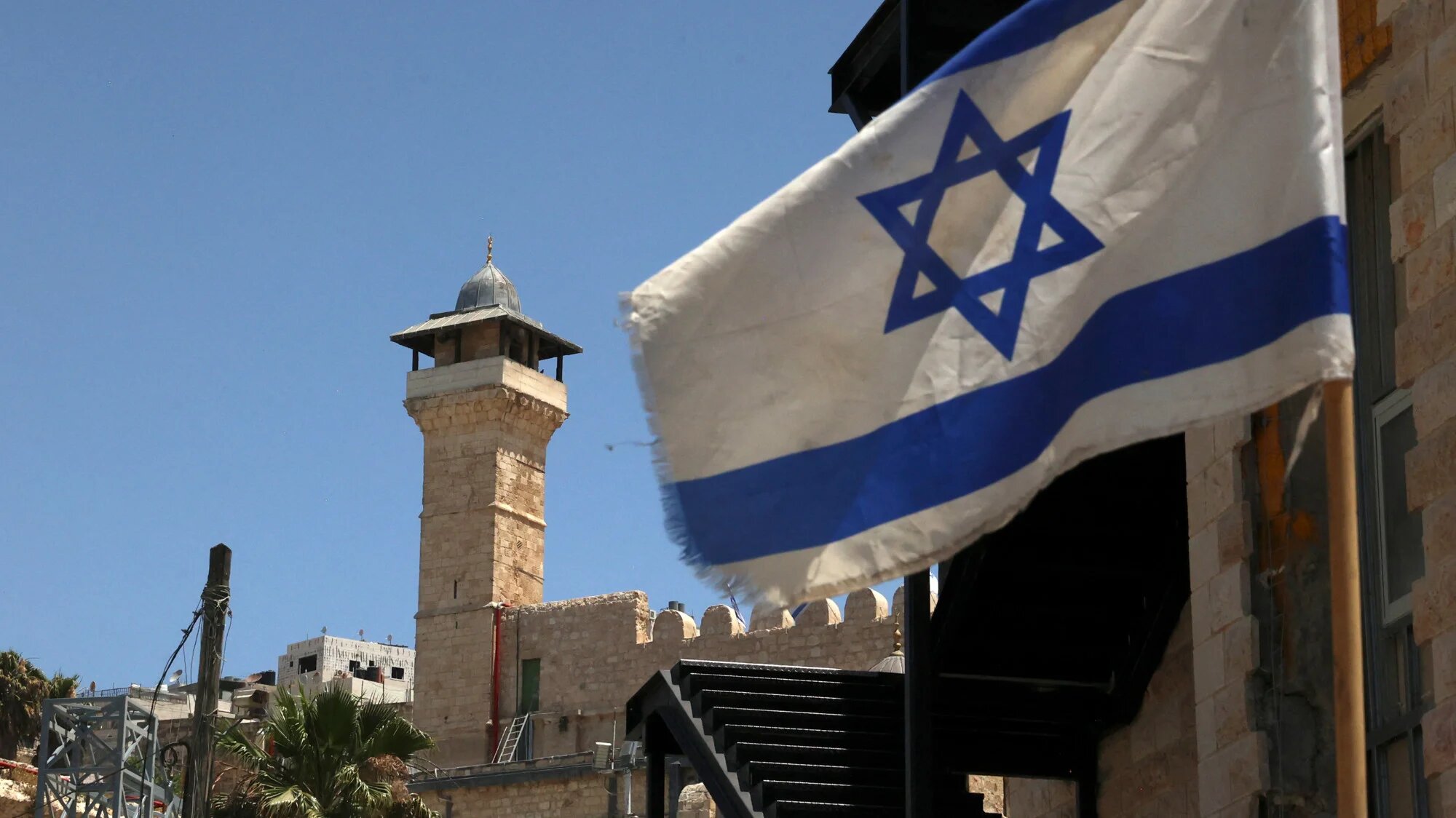 An Israeli flag flies in a street in front of the Ibrahimi Mosque in the occupied West Bank city of Hebron, on 26 May 2022 (AFP/Hazem Bader)