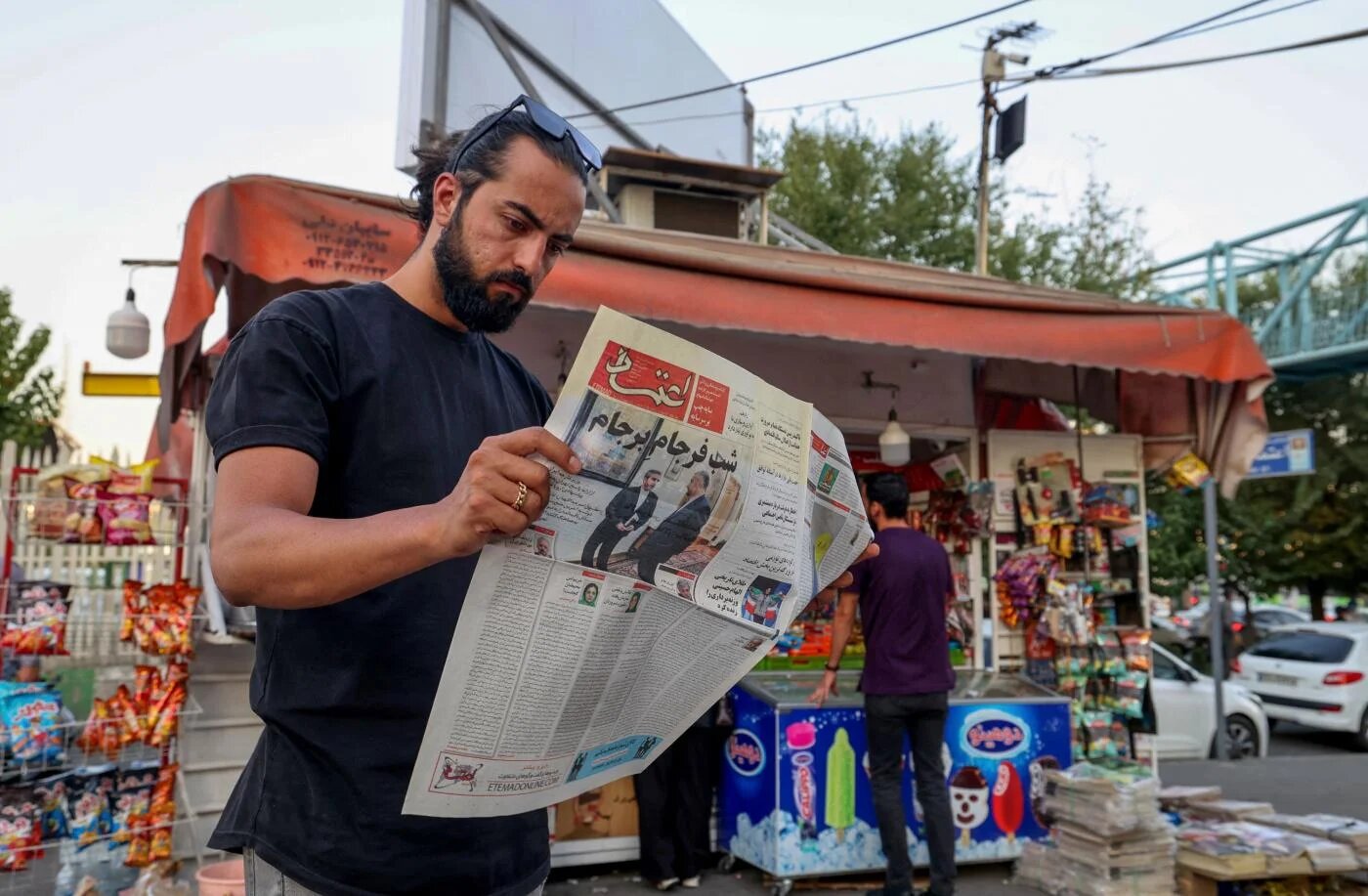 Un homme lit le journal iranien Etemad, dont le titre en une indique en farsi « La nuit de la fin du Plan d’accord conjoint », accompagné d’une photo du ministre iranien des Affaires étrangères Hossein Amir-Abdollahian et de son adjoint Ali Bagheri Kani, chargé des négociations sur le nucléaire, le 16 août 2022 à Téhéran (AFP)