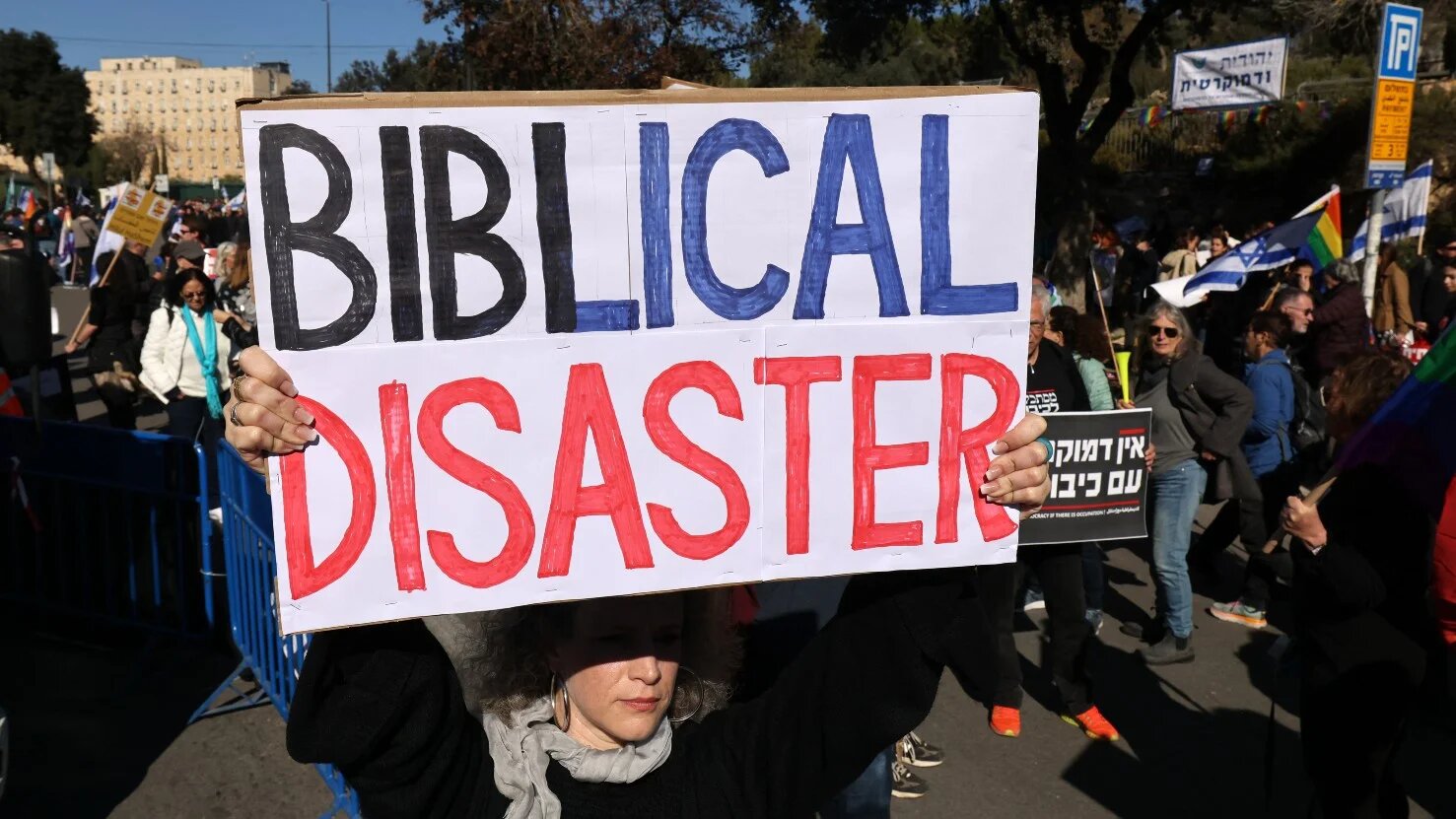 Israeli activists and members of the LGBTQ+ community raise flags and placards as they protest outside parliament on 29 December (AFP)