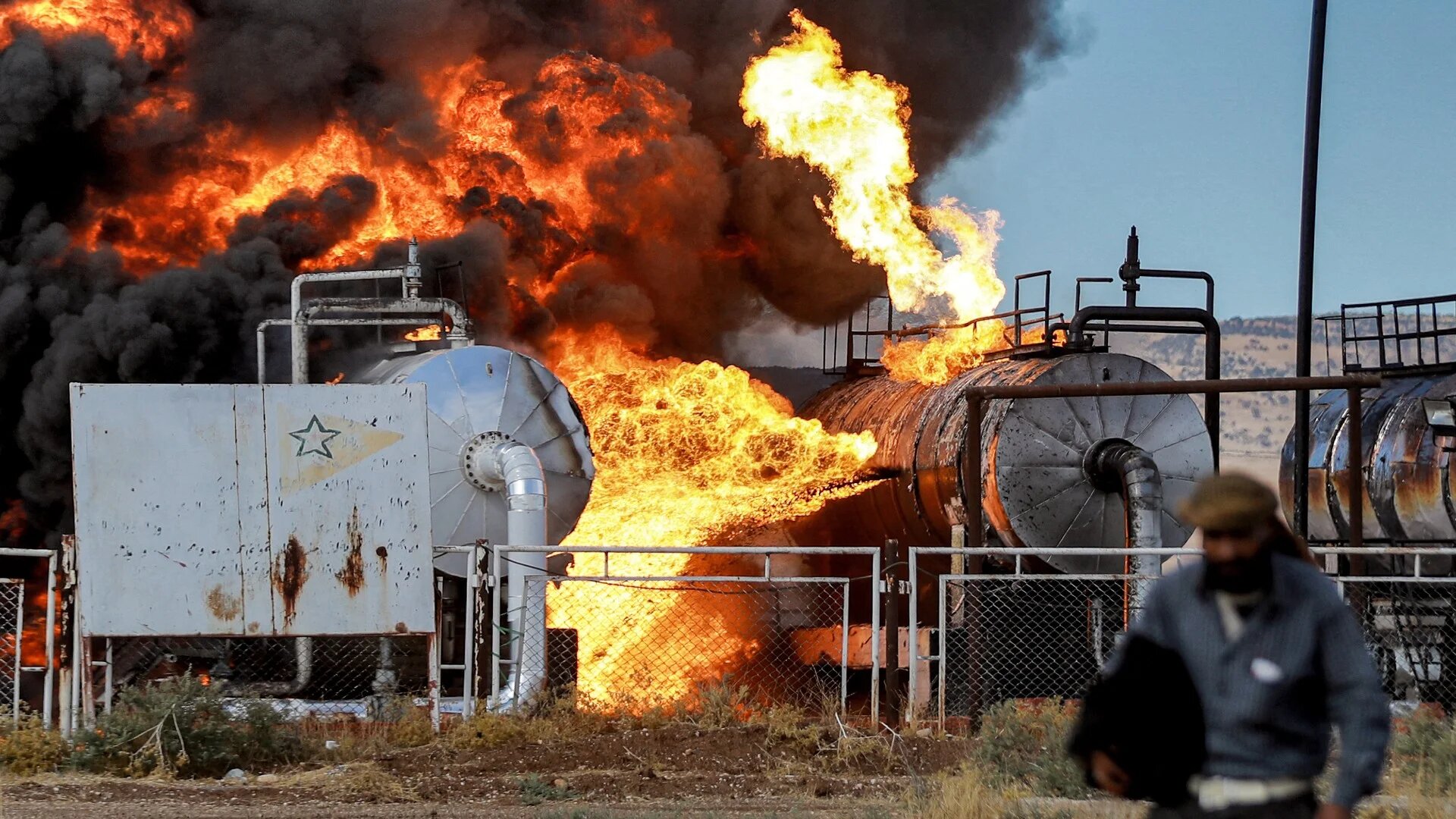 A man walks close to a fire raging at the Zarba oil facility in al-Qahtaniyah following Turkish strikes on 5 October (AFP)
