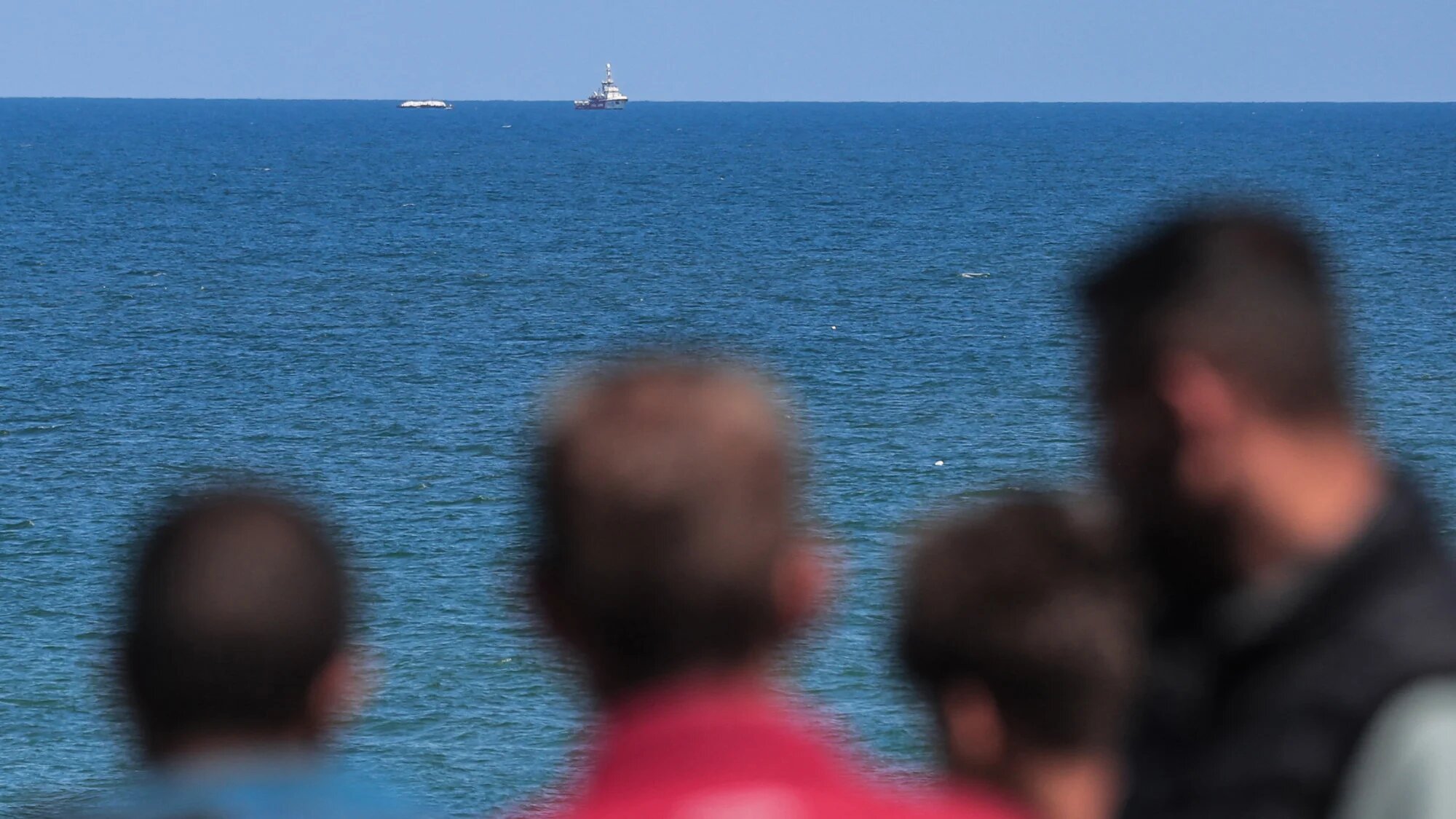 Palestinian men watch as the Open Arms vessel carrying humanitarian aid from Cyprus approaches Gaza City’s coast on 15 March 2024 (AFP)