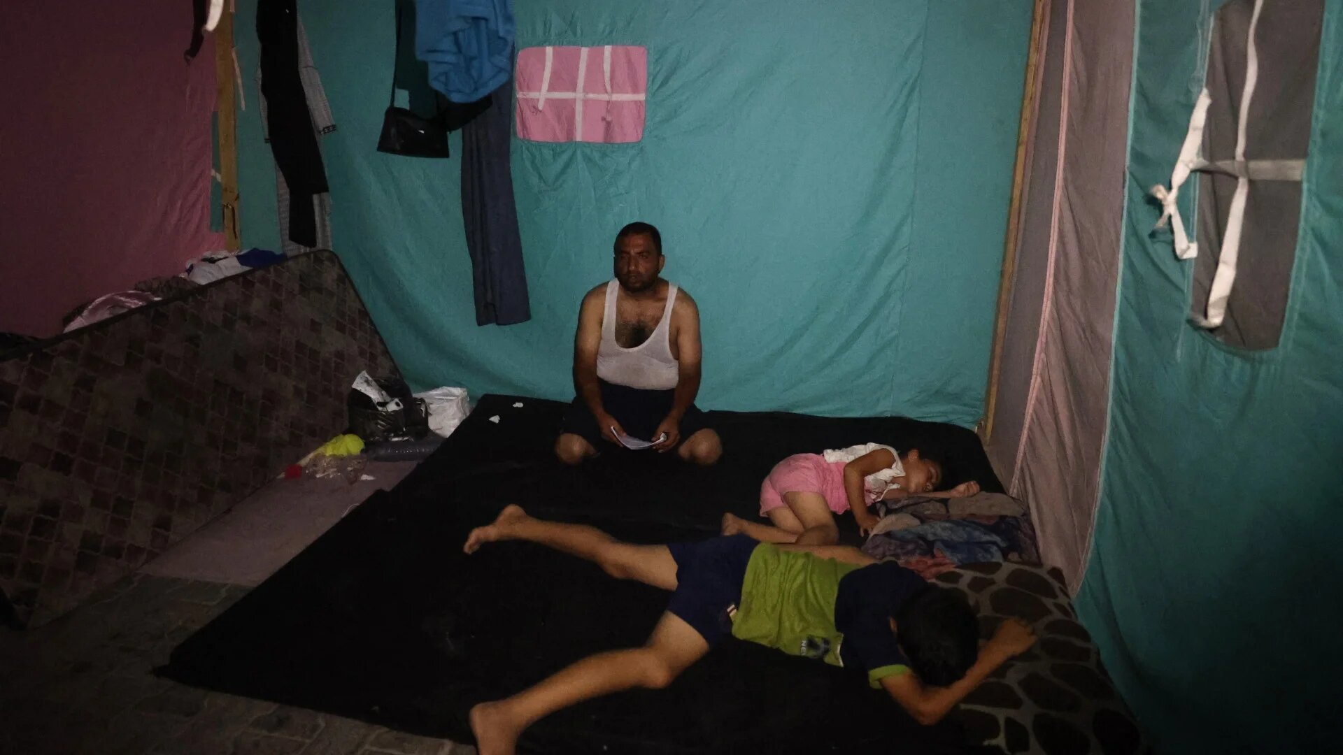 A displaced Palestinian family rests in a tent at night during a heatwave at al-Bureij refugee camp in the central Gaza Strip on 26 June 2024 (Eyad Baba/AFP)
