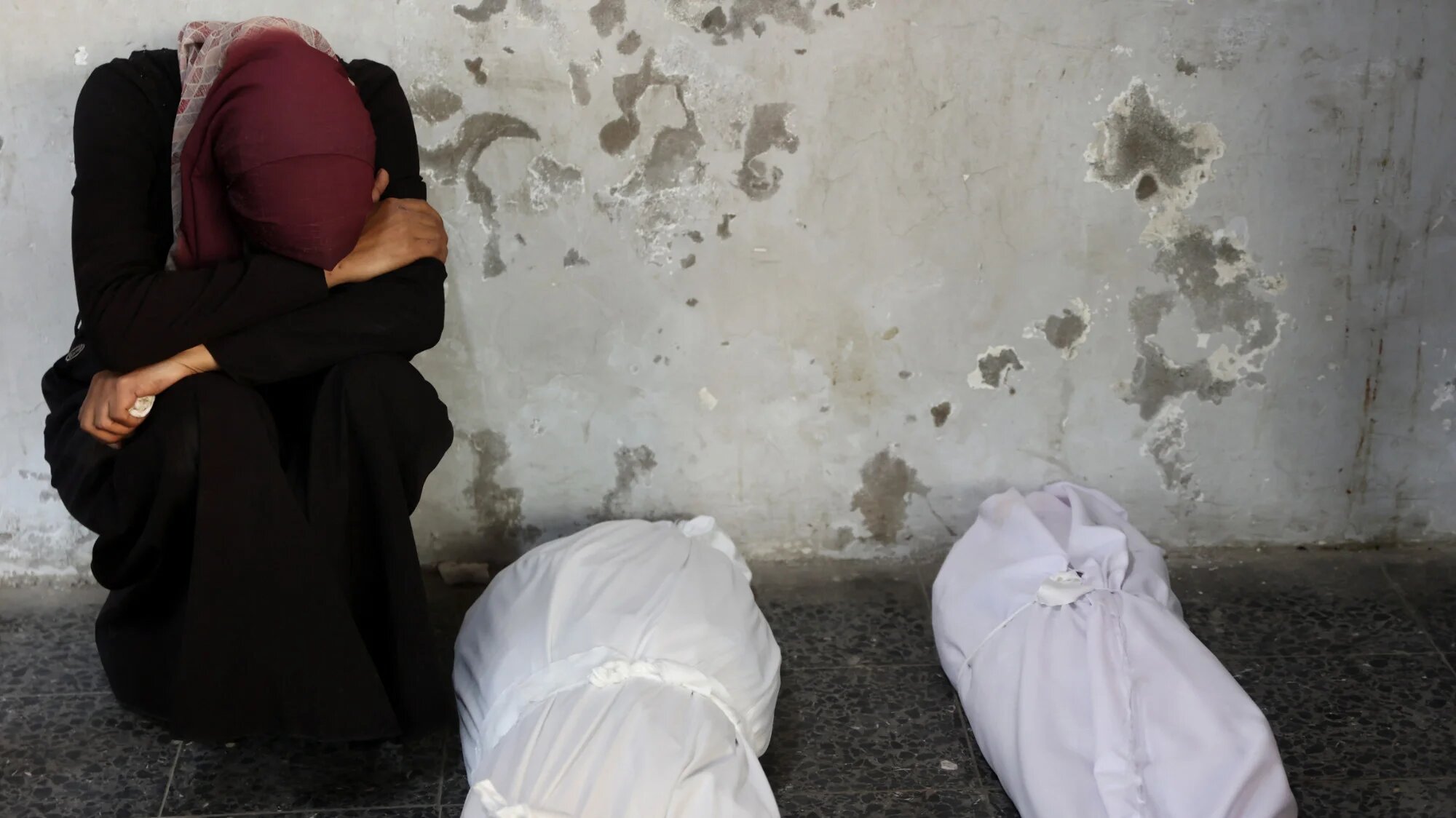 Palestinian woman mourns next to the bodies of loved ones killed in overnight Israeli air strikes on Gaza City at Al-Ahli Arab hospital on 12 December 2024 (AFP/Omar al-Qattaa)