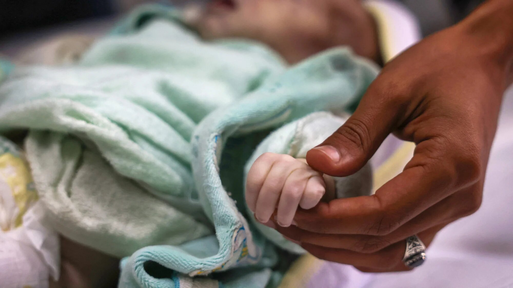A Palestinian man holds the hand of his three-week-old niece, Sila Mahmoud al-Faseeh, who died of hypothermia, in the morgue of Nasser Hospital in Khan Yunis, southern Gaza Strip, on 25 December 2024 (AFP/Bashar Taleb)