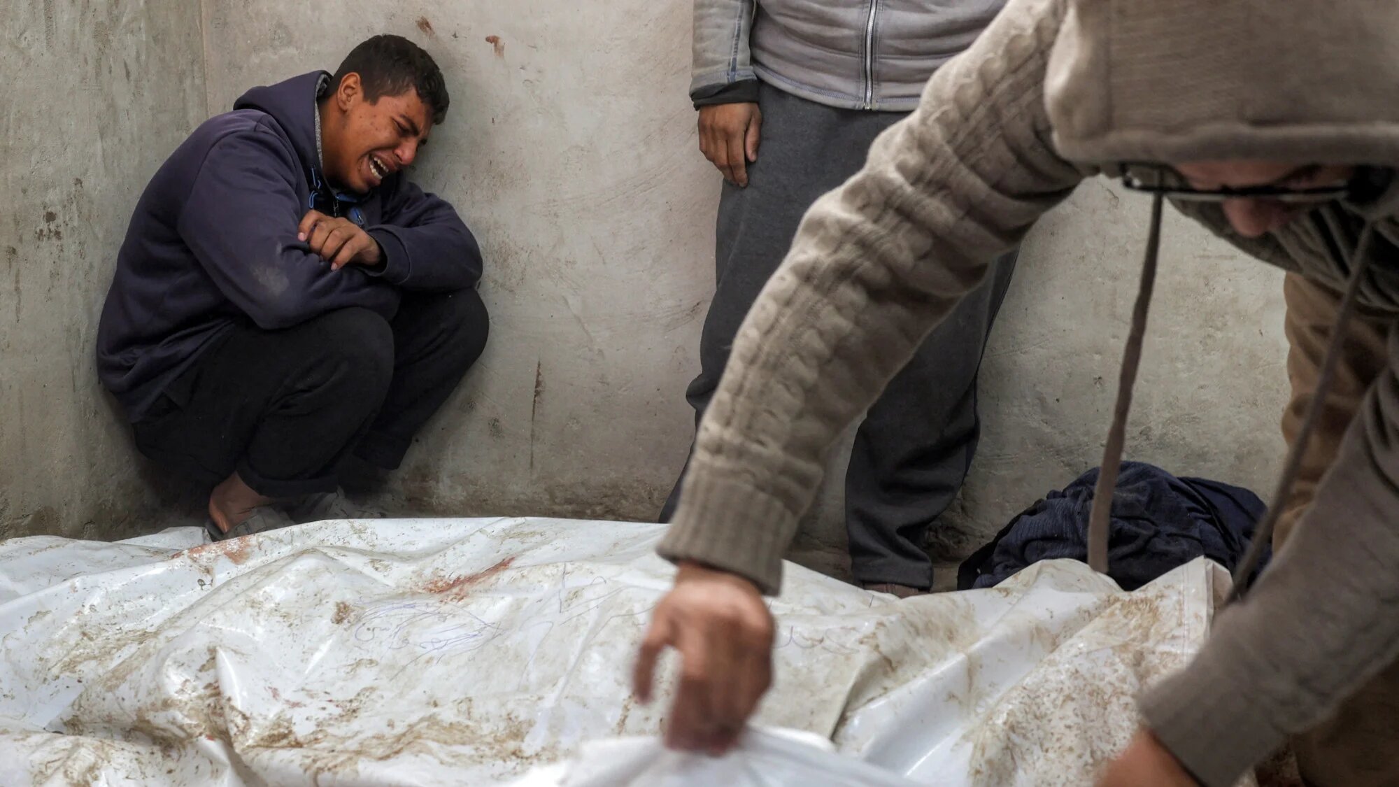 A boy mourns beside the bodies of Palestinians killed by Israeli forces at the morgue of al-Aqsa Martyrs Hospital in Deir al-Balah, central Gaza Strip, on 5 January 2025 (AFP/Eyad Baba)