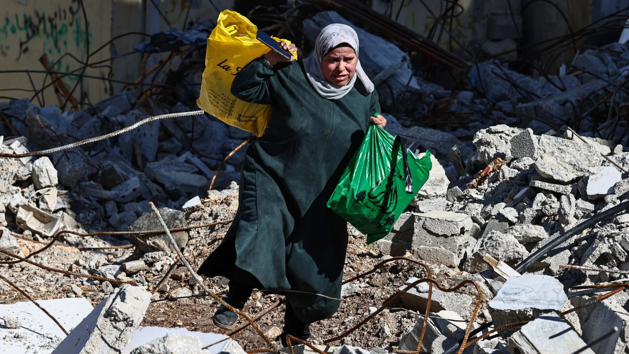 A woman carries bags as she walks on rubble at the Nur Shams camp for Palestinian refugees near Tulkarem amid a weeks-long offensive in the occupied West Bank on 26 February 2025 (AFP/Zain Jaafar)