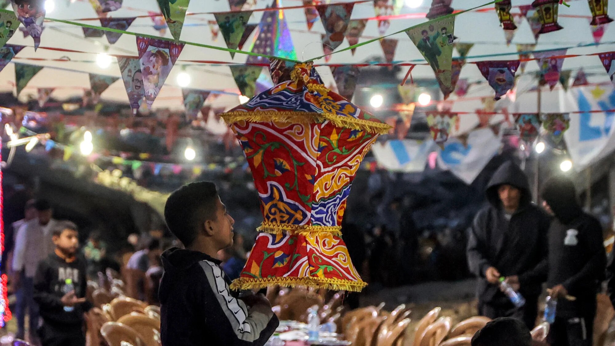 A boy hangs a lantern-shaped decoration ahead of a mass gathering for a communal iftar fast-breaking meal on the second day of the Muslim holy month of Ramadan in the area of al-Dahduh in Gaza City's Tal al-Hawa district on 2 March 2025 (AFP/Omar al-Qattaa)