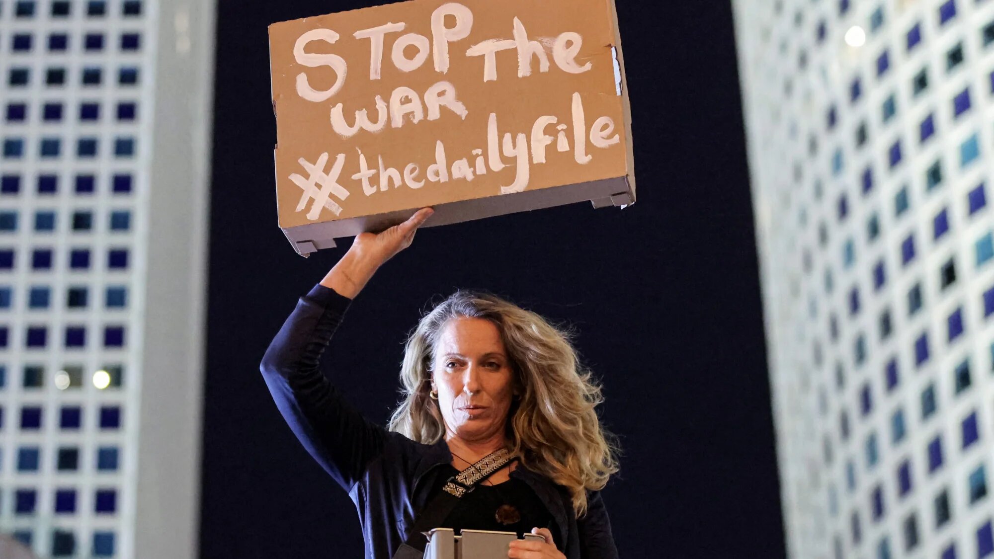 A demonstrator stands on a pole holding a sign during an anti-government protest calling for action to secure the release of Israeli captives outside Azrieli Centre in central Tel Aviv on 5 April 2025 (AFP/Jack Guez)