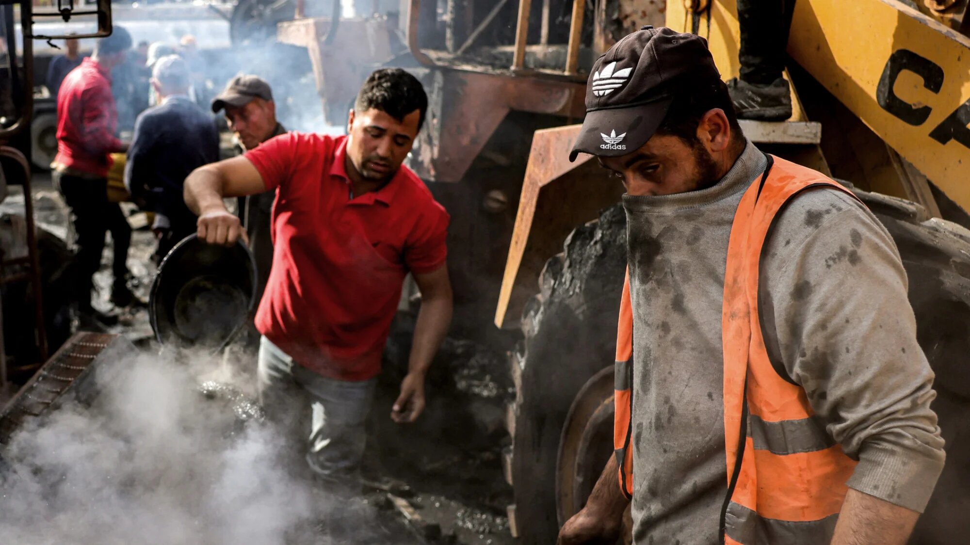 A man covers his nose as he and another try to extinguish a smouldering fire at Jabalia municipality’s bulldozer garage, hit by Israeli strikes on 22 April 2025 (AFP/Basahr Taleb)