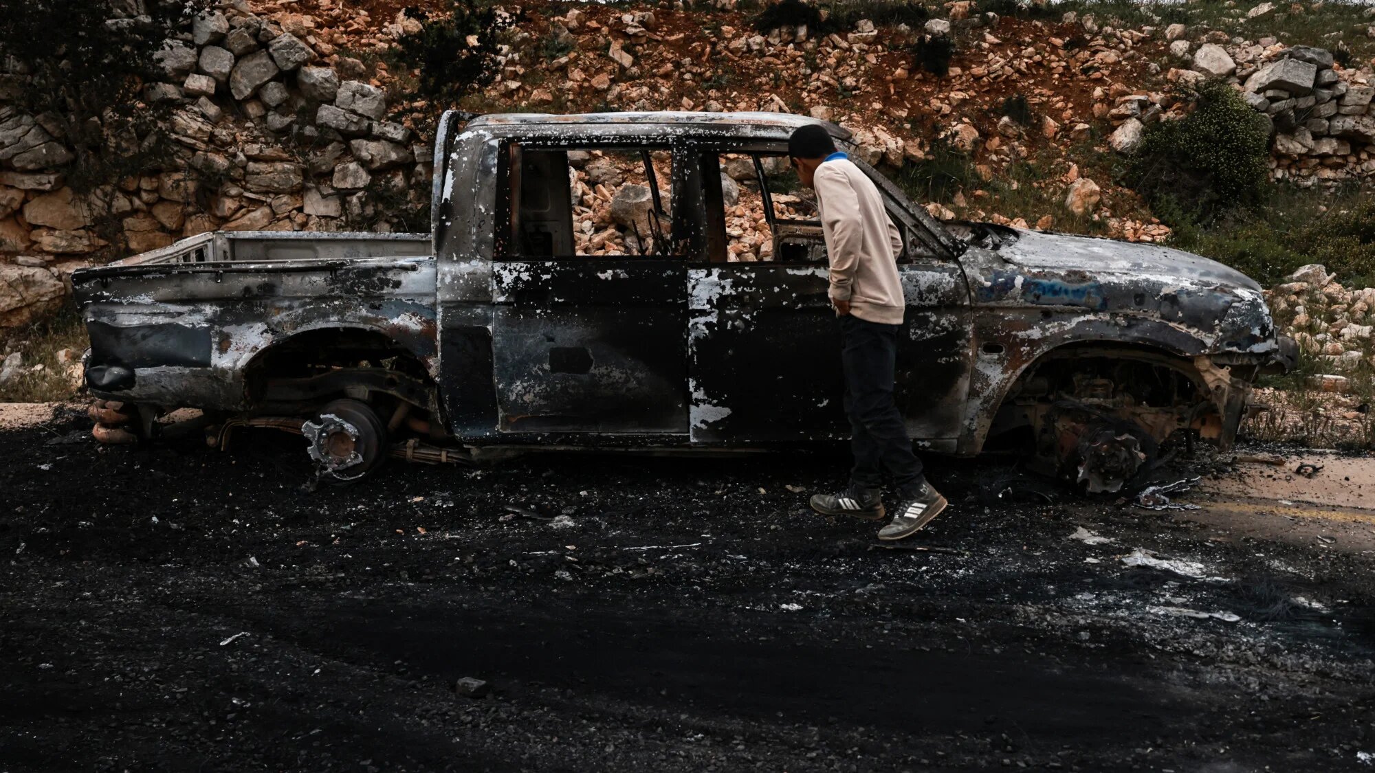 A man inspects a charred car following an attack by Israeli settlers in the village of Sinjil, north of the occupied West Bank city of Ramallah, on 23 April 2025 (AFP/Zain Jaafar)
