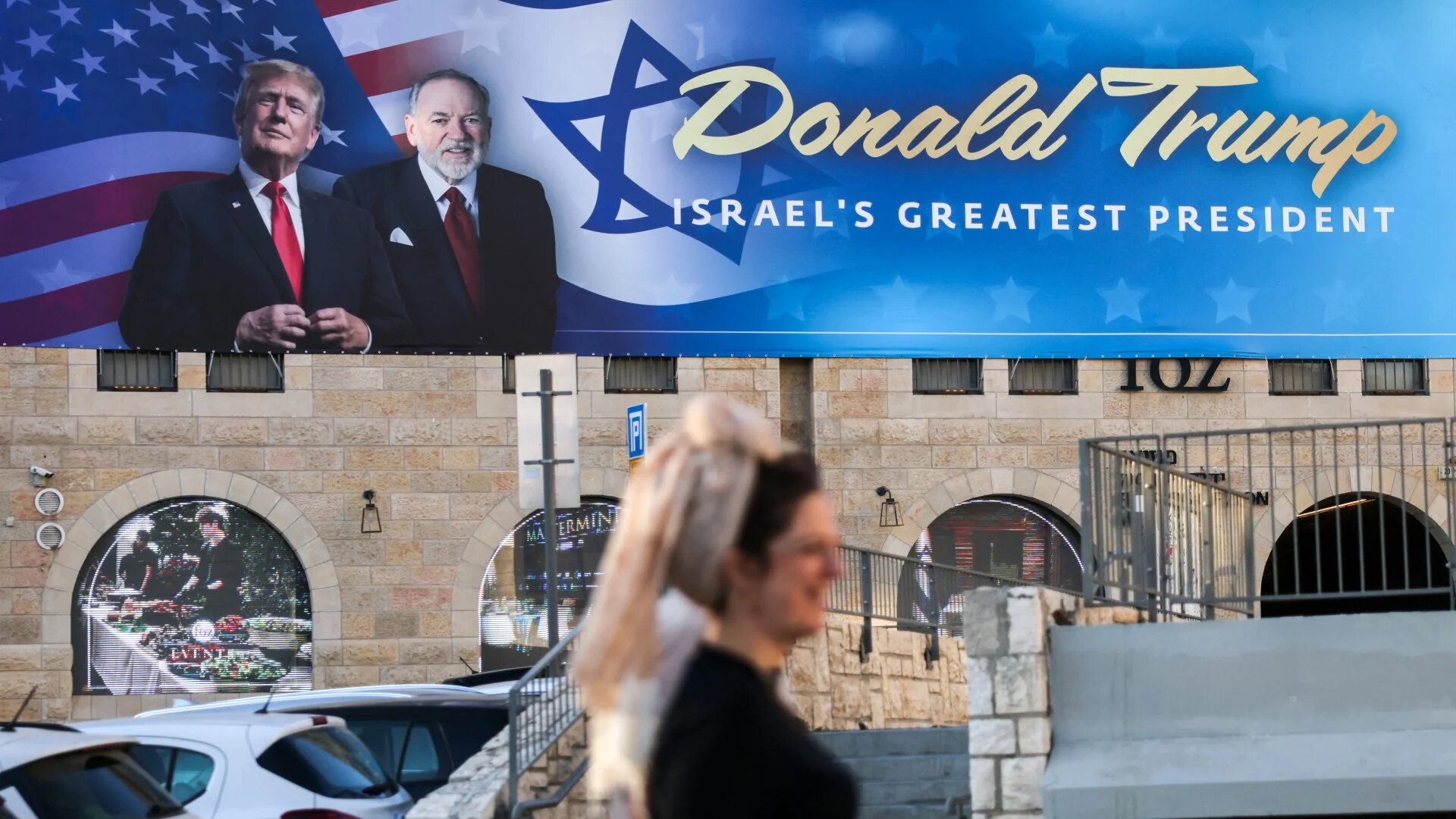 A banner featuring Donald Trump and US Ambassador to Israel Mike Huckabee is displayed in central Jerusalem, 7 May 2025 (Ahmad Gharabli/AFP)